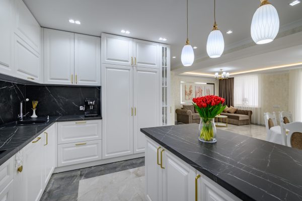 Large black and white expensive well-designed modern kitchen in studio interior, black marble countertop on kitchen island with bouquet of red flowers